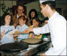 Un cuisinier bénévole prépare des crêpes devant un groupe d’enfants et d’adultes attentifs